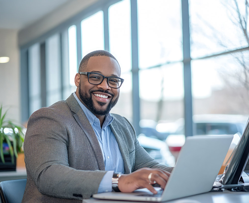 Smiling finance manager sitting at a laptop in the showroom