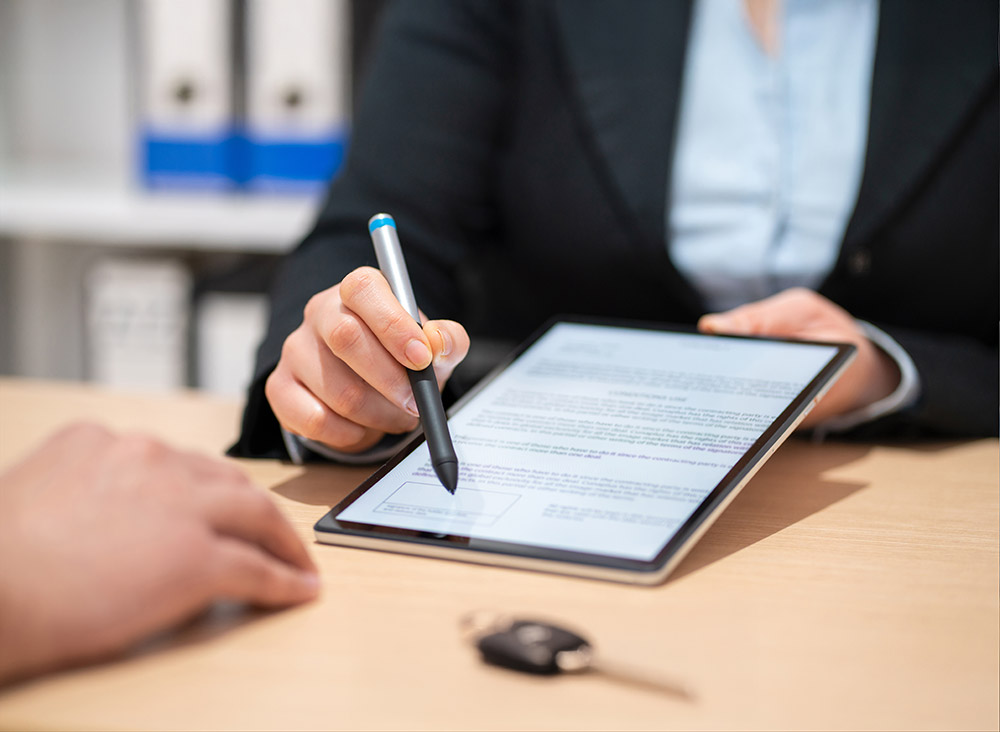 A finance manager closing a deal handing an electronic pen to a buyer to sign on a tablet