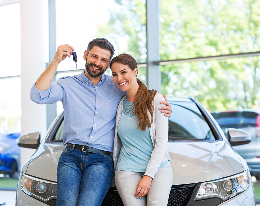Couple in the showroom holding keys infront of their new car smiling