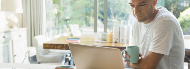 Man working in kitchen with laptop learning about personal loans and credit card debt