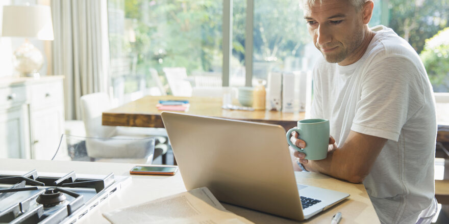 Man working in kitchen with laptop learning about personal loans and credit card debt