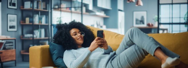 Woman lounging on couch looking at her cell phone and searching for online personal loans.