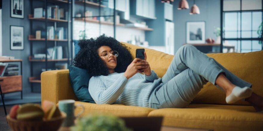 Woman lounging on couch looking at her cell phone and searching for online personal loans.