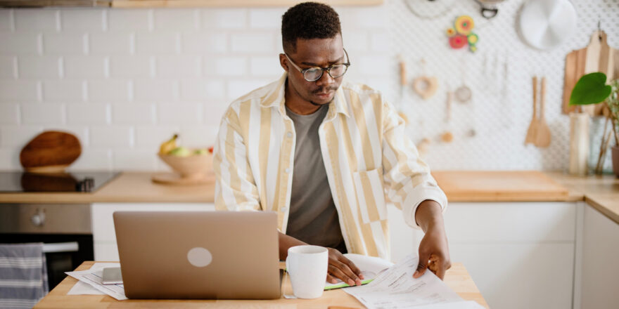 A man wearing glasses working at a table in his kitchen.