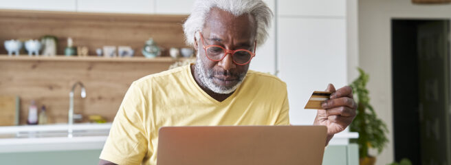Senior man with red glasses looking at laptop with a credit card to learn about debt consolidation loan