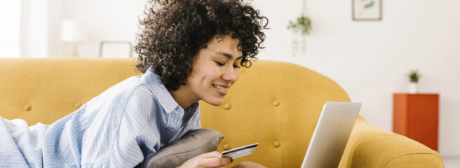 Woman on yellow sofa with laptop holding a credit card