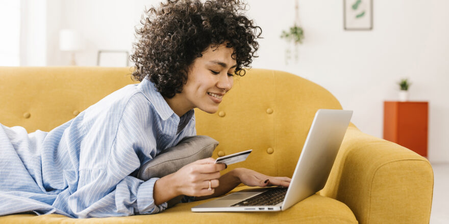 Woman on yellow sofa with laptop holding a credit card