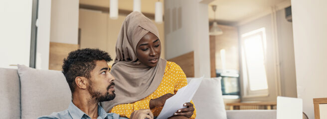 Young muslim African family of two managing finances at home, reviewing bank accounts, sitting with notebook computer. Wife and husband paying taxes online on laptop.
