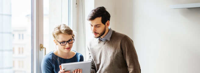 Two young business people standing by a window and looking at a digital tablet