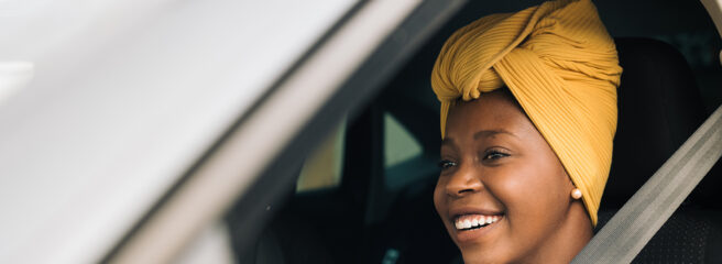 A smiling woman driving her car with the window down.