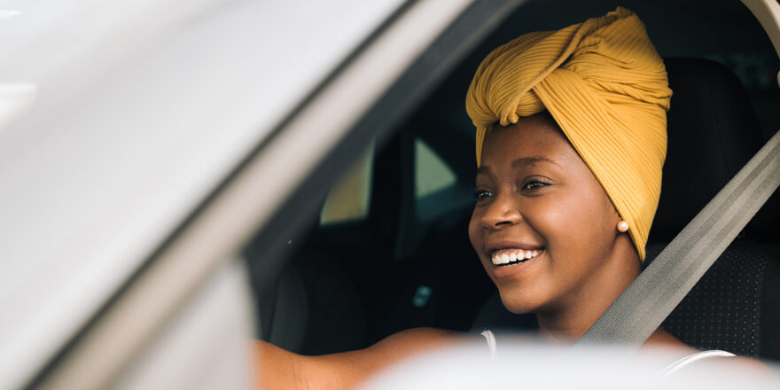 A smiling woman driving her car with the window down.