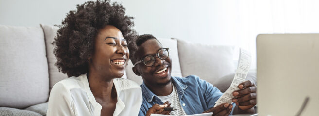 Family insurance concept. Positive black couple reading documentation at home, checking agreement details together. Young African Couple Sitting On Sofa Calculating Invoice