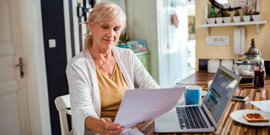 Senior woman in front of computer comparing unsecured and secured personal loans with paperwork in hand.