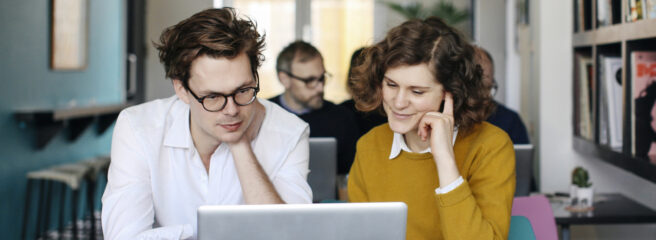 A man sitting next to a woman is sitting in a cafe at a table looking at a laptop going over the rise in interest rates.