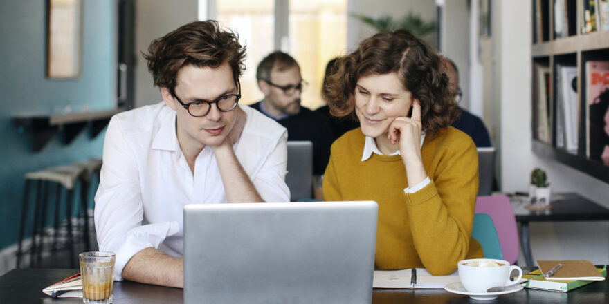 A man sitting next to a woman is sitting in a cafe at a table looking at a laptop going over the rise in interest rates.