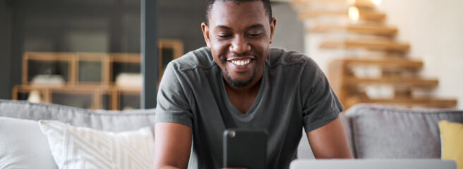 Man sitting on couch looking at iPhone working on refinancing a loan.