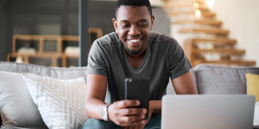 Man sitting on couch looking at iPhone working on refinancing a loan.