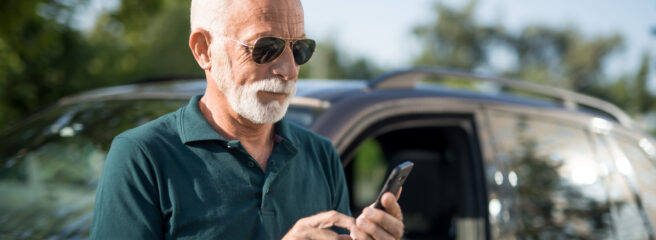 Man leaning on black car using his cell phone to learn about how to pay off a car loan early.