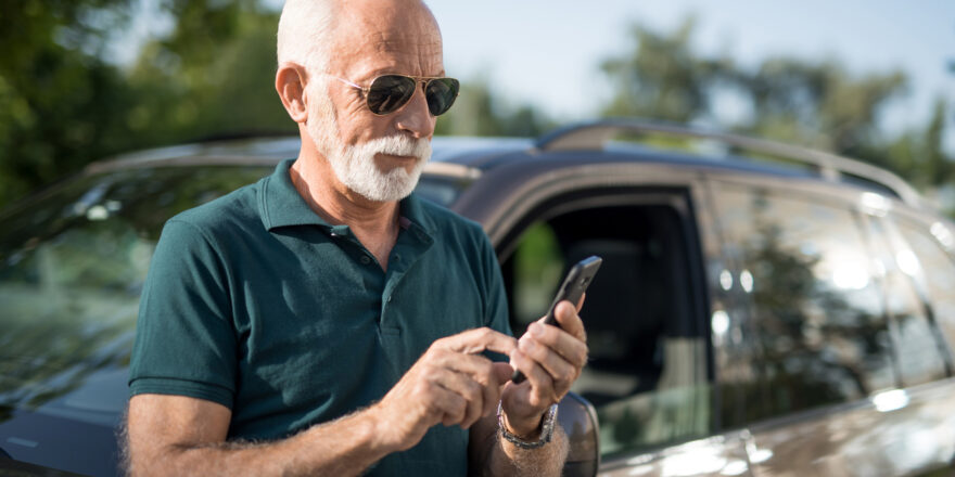 Man leaning on black car using his cell phone to learn about how to pay off a car loan early.