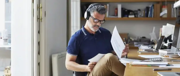 Man wearing headphones at his desk reviewing papers on debt consolidation.