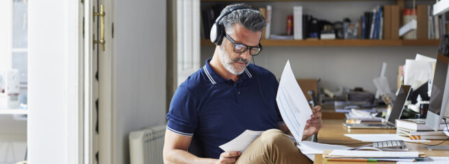 Man wearing headphones at his desk reviewing papers on debt consolidation.