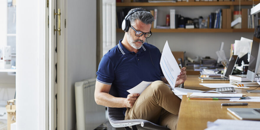 Man wearing headphones at his desk reviewing papers on debt consolidation.