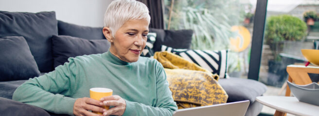 Older woman looking at laptop screen holding a yellow cup.