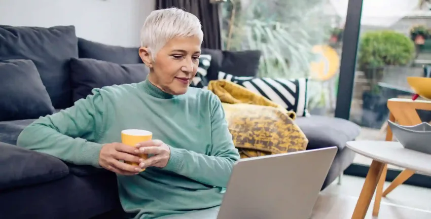 Older woman looking at laptop screen holding a yellow cup.