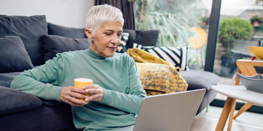 Older woman looking at laptop screen holding a yellow cup.