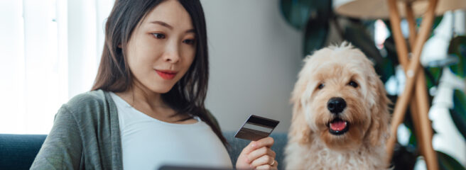 Woman sitting next to dog holding a credit card and looking at her laptop.