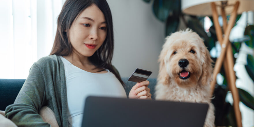 Woman sitting next to dog holding a credit card and looking at her laptop.