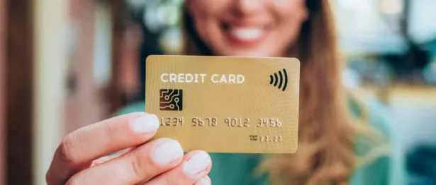 Woman with blonde hair in green shirt holding a gold balance transfer credit card.