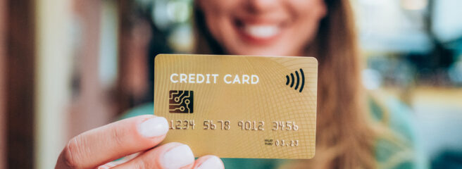 Woman with blonde hair in green shirt holding a gold balance transfer credit card.