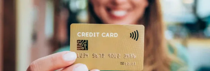 Woman with blonde hair in green shirt holding a gold balance transfer credit card.