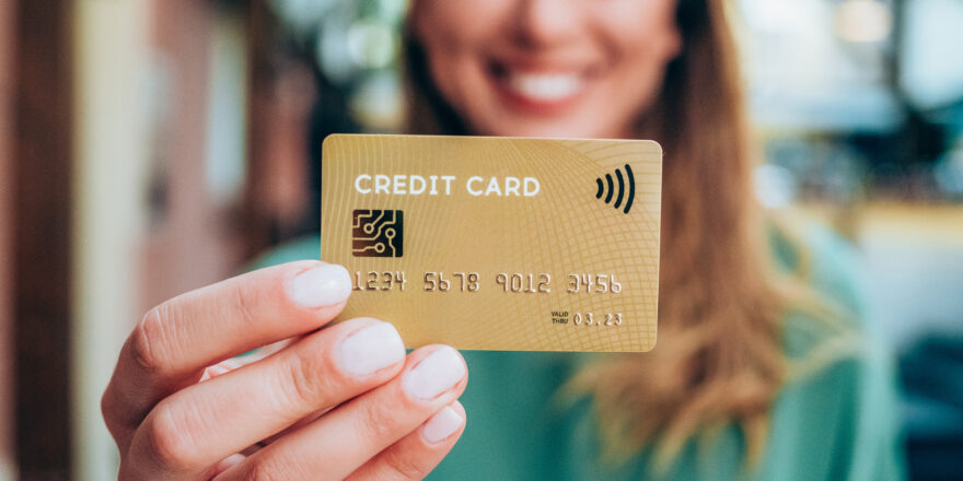 Woman with blonde hair in green shirt holding a gold balance transfer credit card.