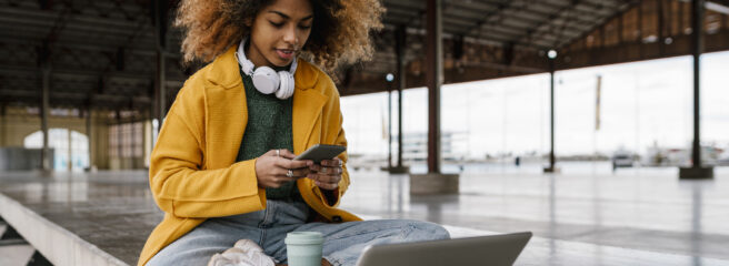 Woman sitting on bench with cell phone and laptop researching safe emergency loans.