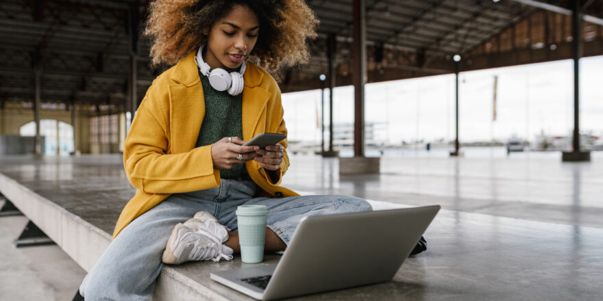 Woman sitting on bench with cell phone and laptop researching safe emergency loans.