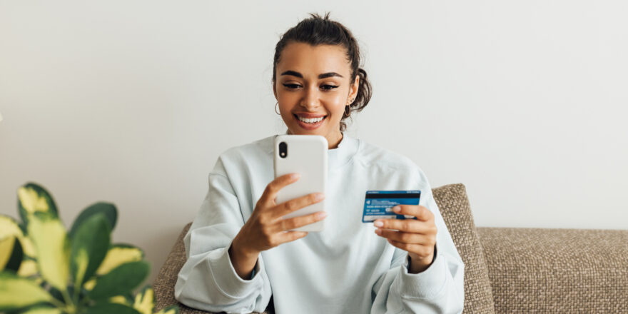 Woman sitting on her couch using her cellphone to search for details on credit card refinancing.