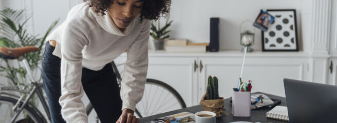 Woman standing in her apartment and writing down notes to calculate her debt-to-income ratio.