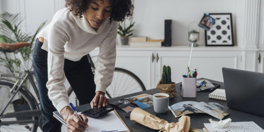 Woman standing in her apartment and writing down notes to calculate her debt-to-income ratio.