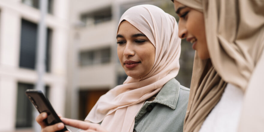 Two women sitting outside researching no-credit-check personal loans on a cellphone.