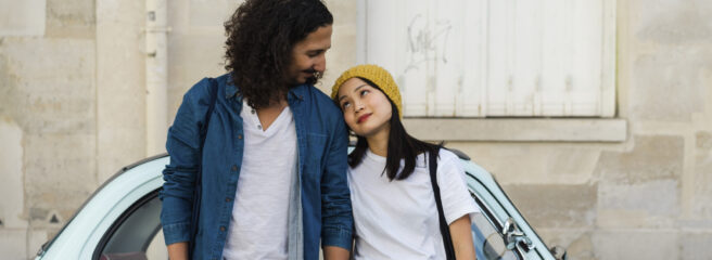 Young couple holding hands and leaning back on a small blue car