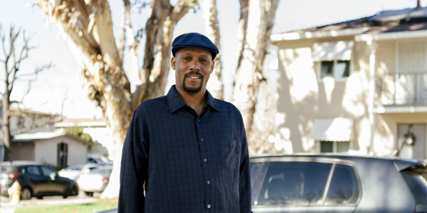 Man in dark blue long sleeve shirt with hat standing in front of car