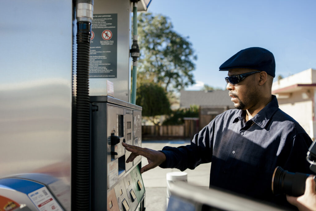 Man in hat with a dark blue shirt paying for gas at the pump