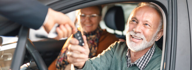 A couple sits in their new car and accepts the keys from a car salesperson