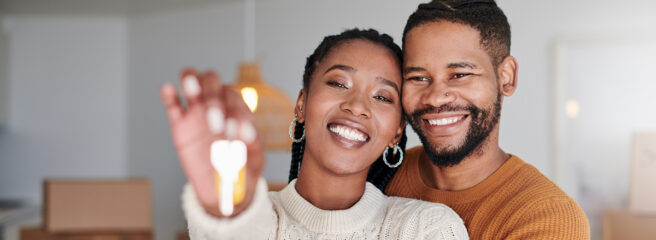 Couple stands in their new living room and holds the keys to their new home