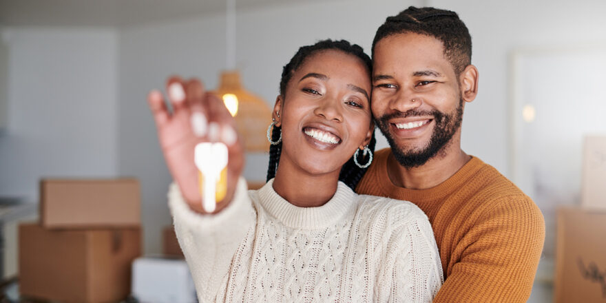 Couple stands in their new living room and holds the keys to their new home