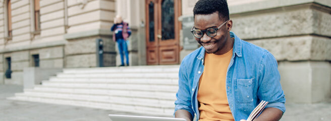 Man in orange shirt and blue button down working outside on laptop