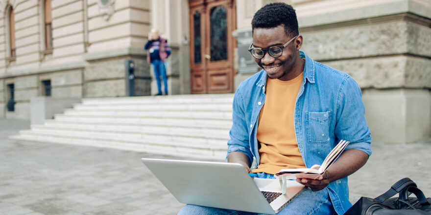 Man in orange shirt and blue button down working outside on laptop