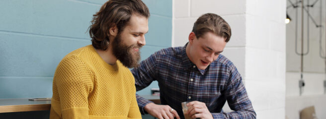 Two men research inflation on a laptop while sitting on bar stools